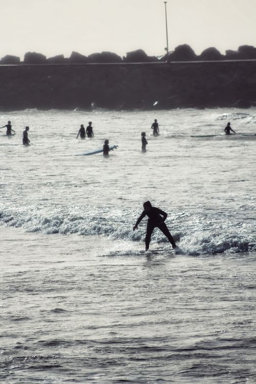 Free Surfers riding waves at sunset near the shoreline with a silhouette backdrop. Stock Photo