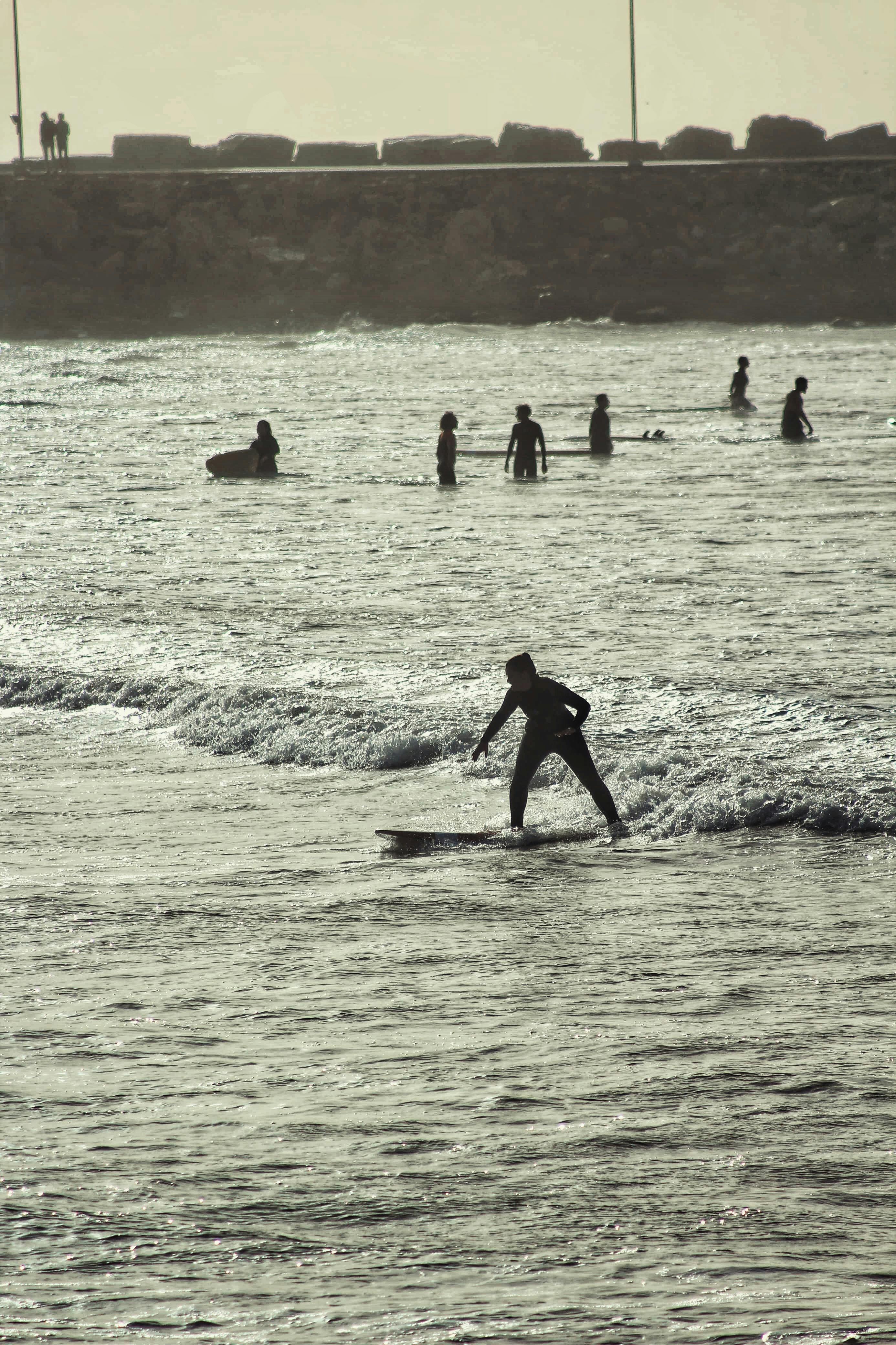 A surfer catching a wave at sunset with silhouettes of people in the background.