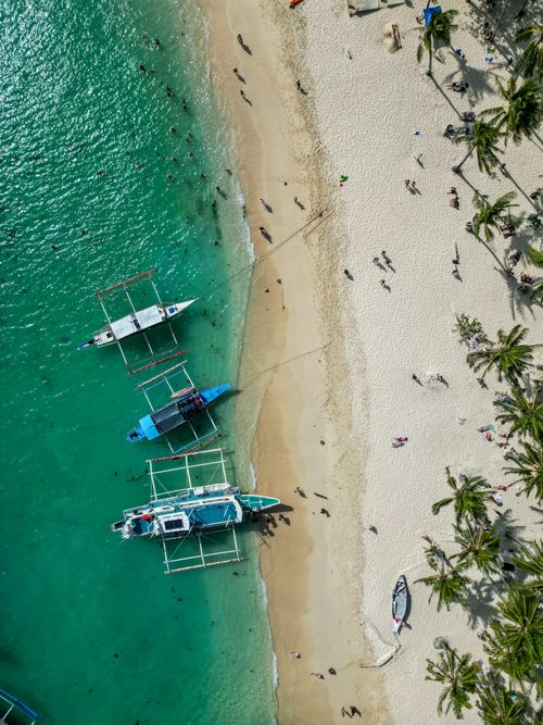 Free Stunning aerial shot of a sandy beach in the Philippines with traditional boats and palm trees. Stock Photo