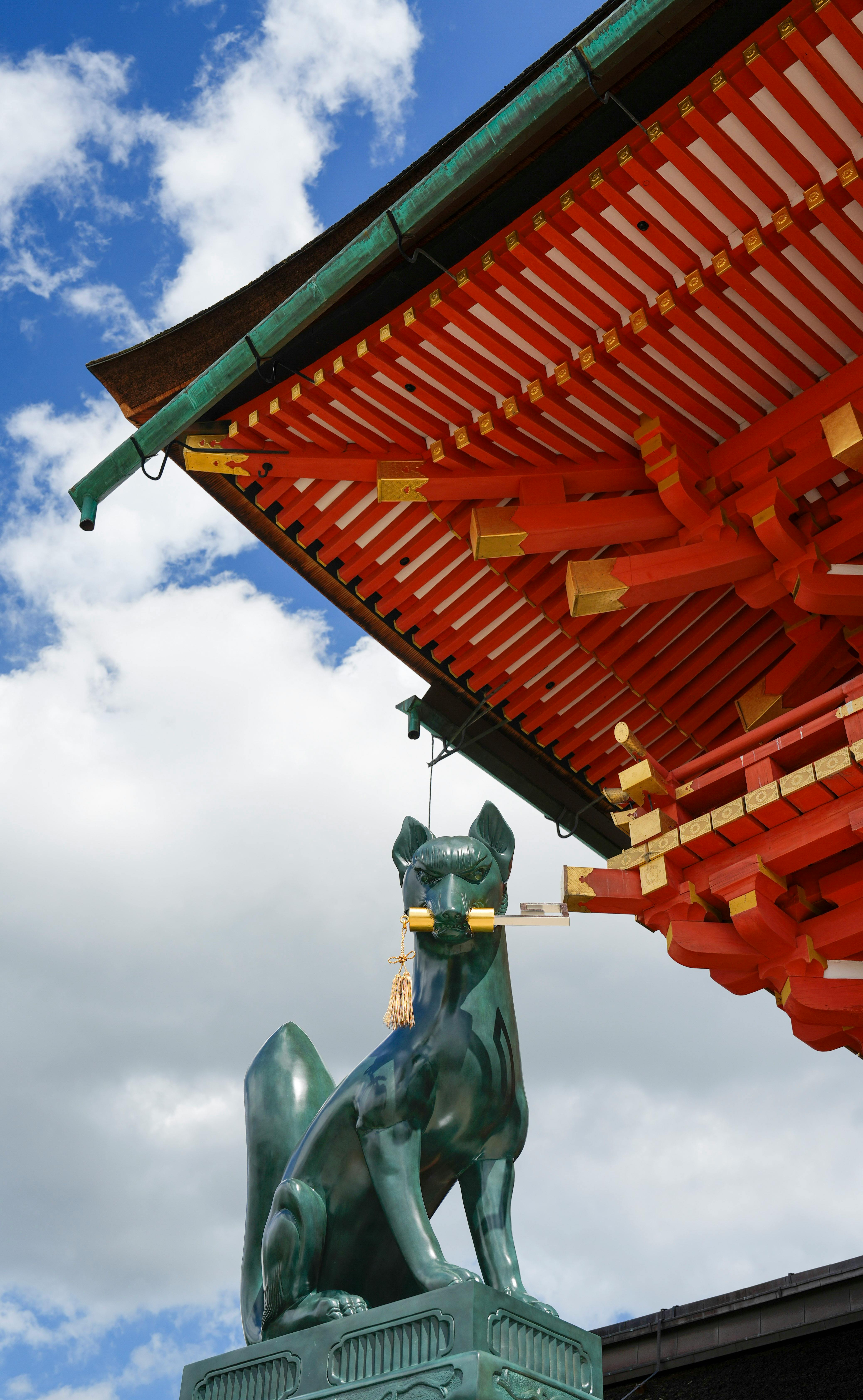 Elevated view of a red shrine rooftop and Kitsune statue at Fushimi Inari Taisha in Kyoto, Japan.