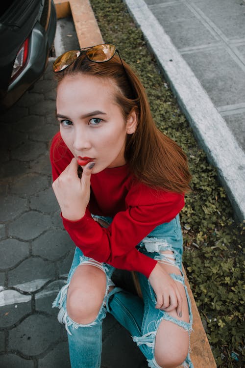 Frau Im Roten Pullover Und In Den Blauen Distressed Jeans, Die Draußen Sitzen