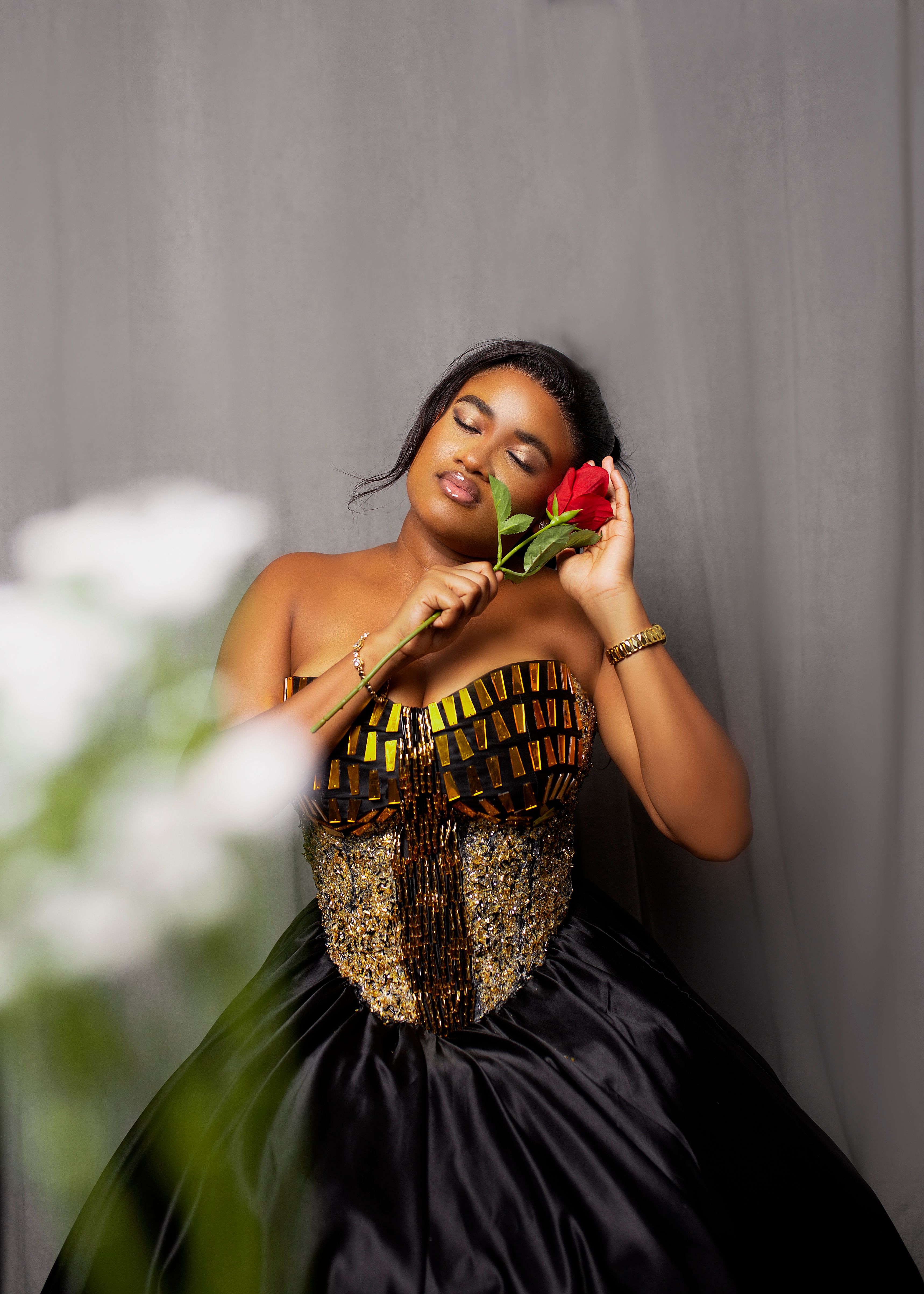 Graceful woman in elegant dress holding a red rose, exuding beauty and serenity indoors.