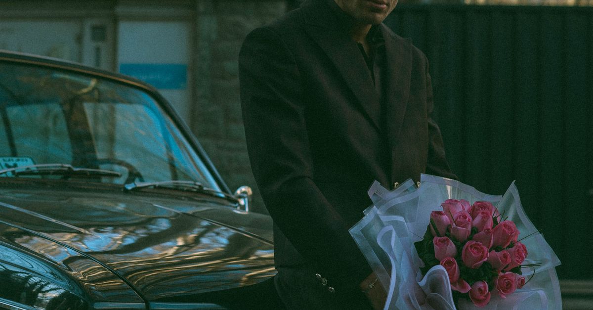 Rüyada Tanımadığınız Birinden Romantik Hediye Almak - Rüya Tabiri ve Anlamı - A stylish man in sunglasses leans on a vintage car holding pink roses, exuding a mysterious charm.