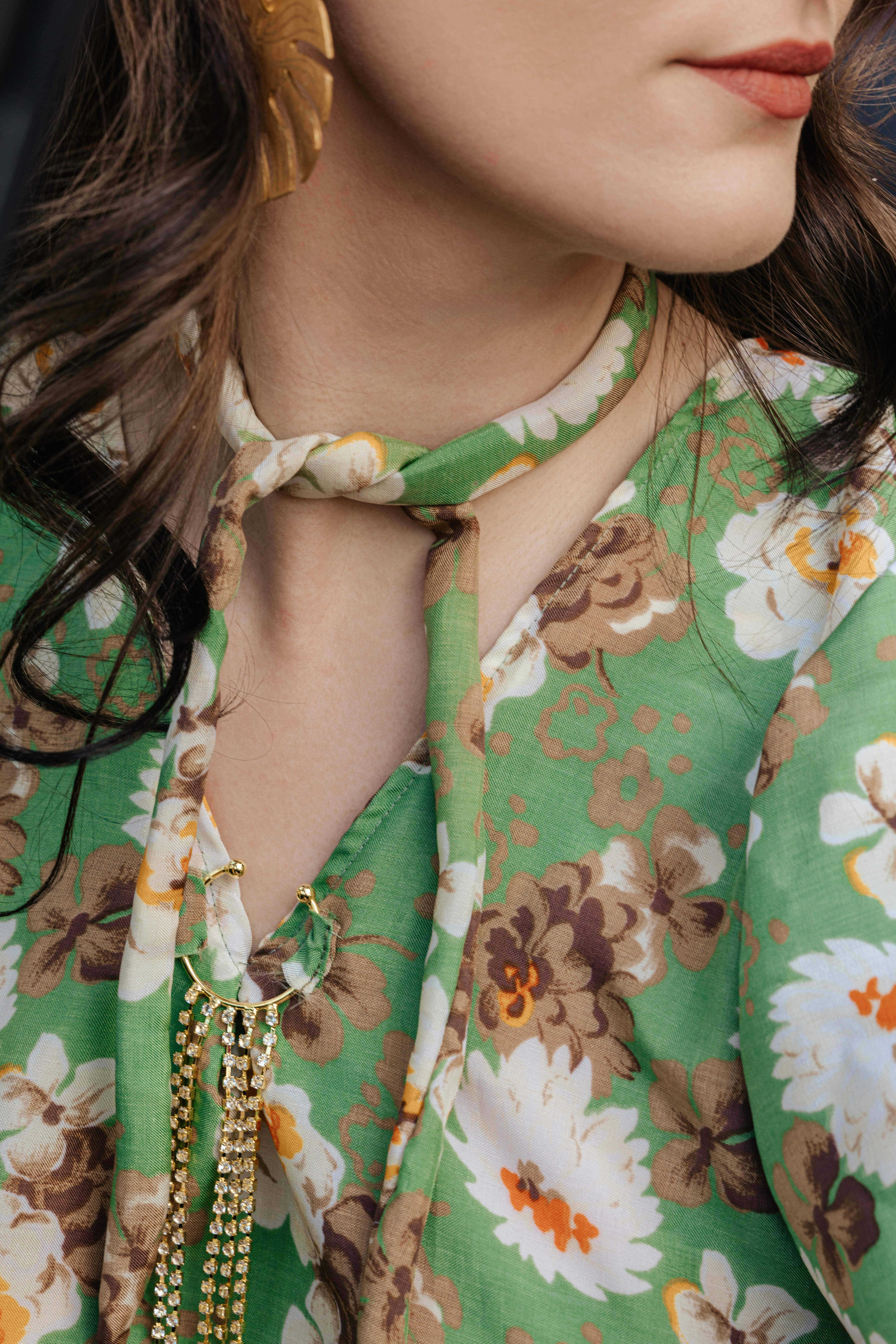Elegant close-up of a floral dress with gold chain jewelry and leaf earring, exuding sophistication.