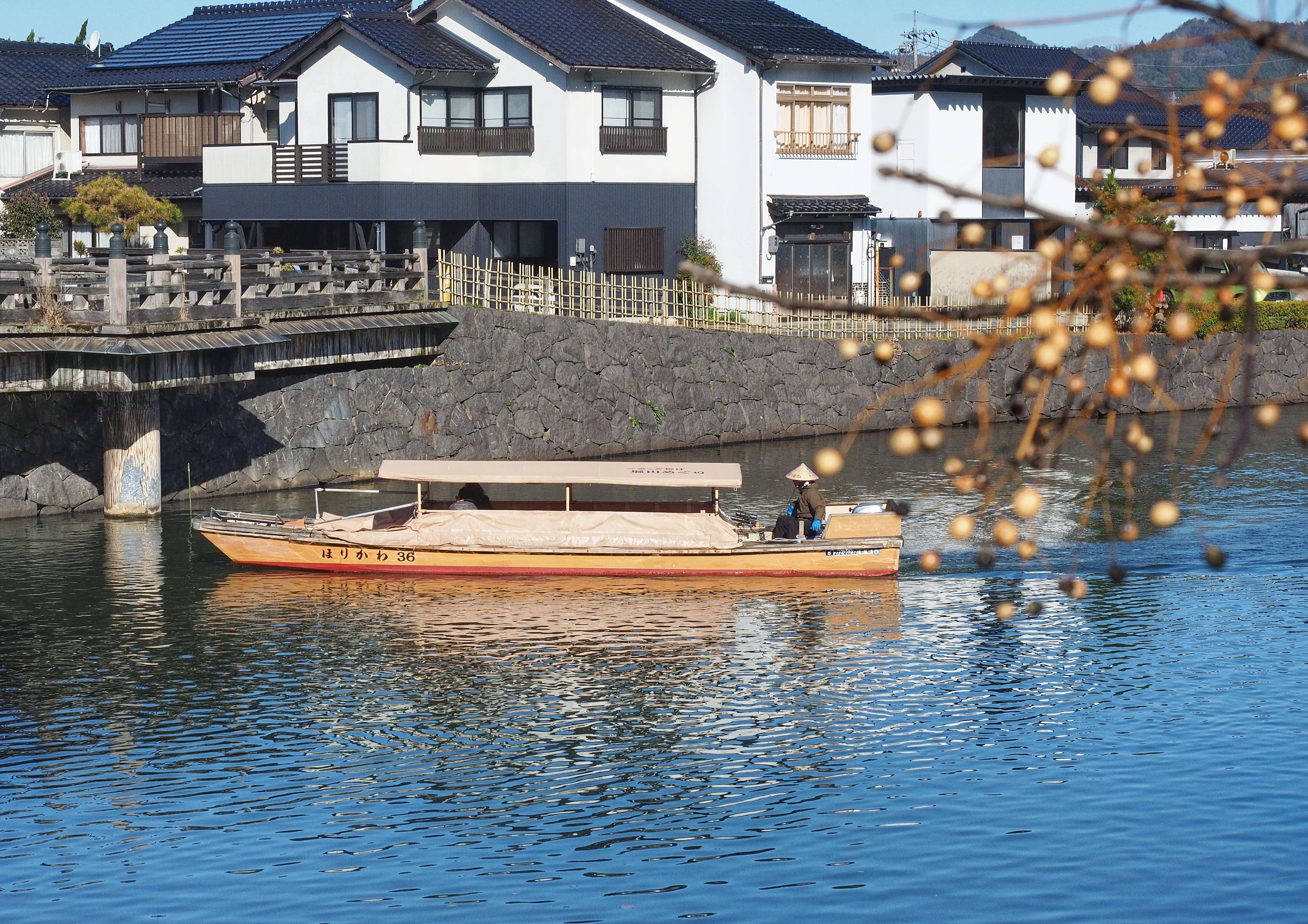 A scenic view of a traditional boat gliding on a calm river by Japanese houses.