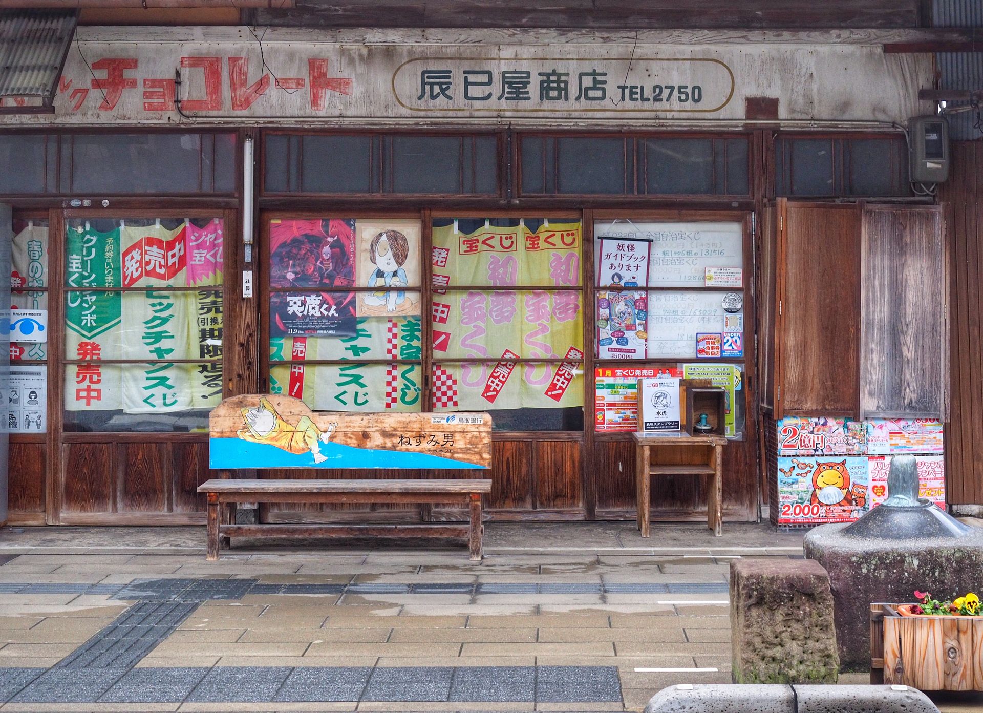 Vintage Japanese storefront with colorful, weathered signage and wooden bench on a rainy day.