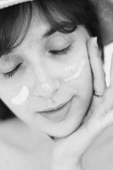Black and white portrait of a woman applying skincare cream. Relaxed and serene.
