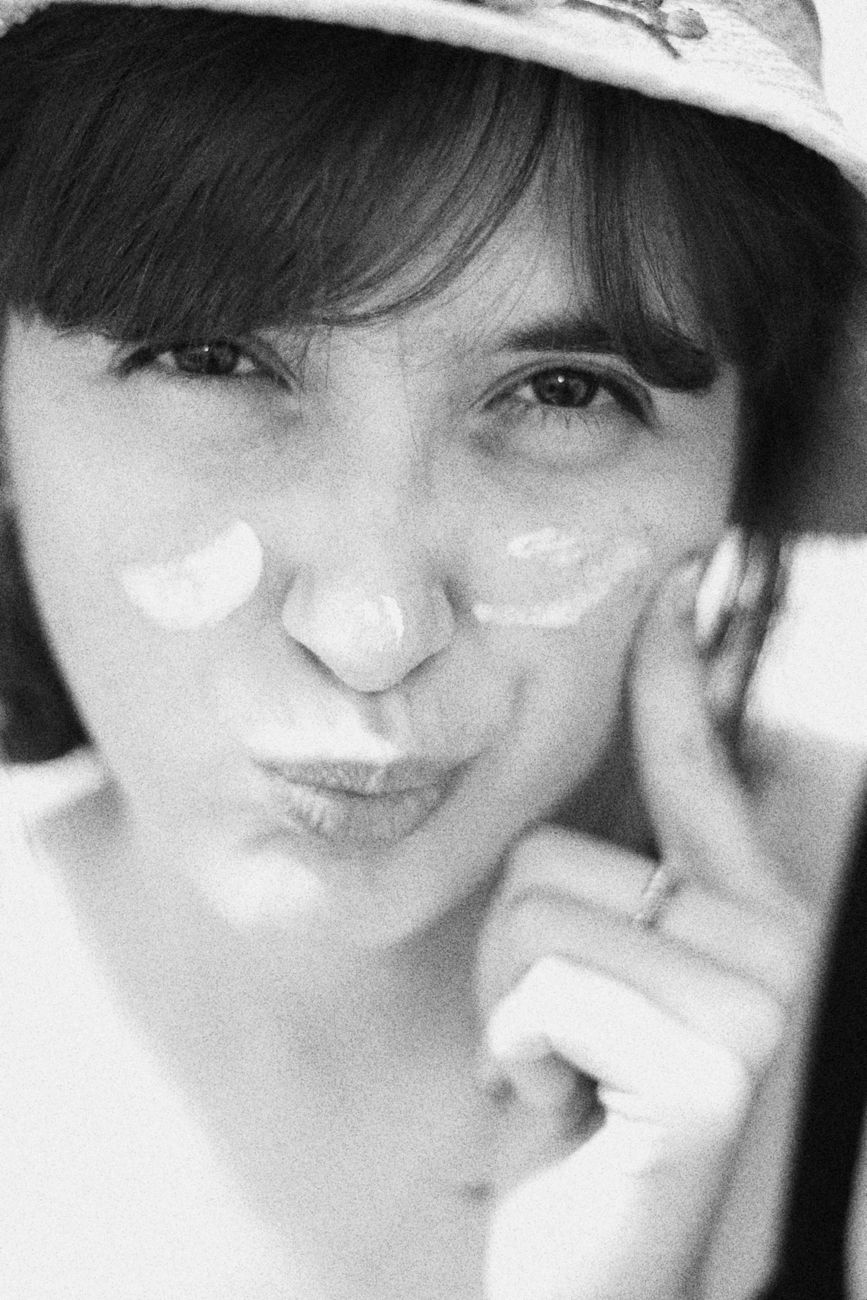 A playful black and white portrait of a woman applying cream on her face outdoors.