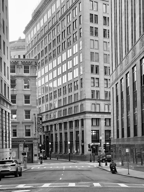 Free Black and white photo of an urban street flanked by classic tall office buildings. Stock Photo