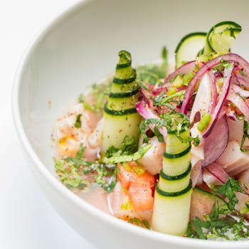 Delightful ceviche garnished with cucumber spirals and red onion. A fresh culinary treat.