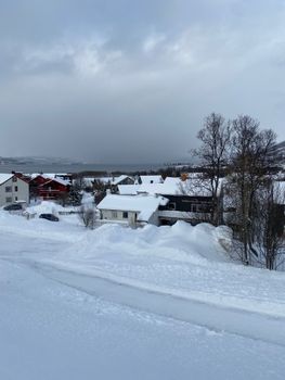 A picturesque view of Tromsø, Norway, showcasing snow-covered houses and trees in the winter season.