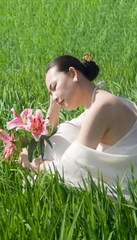 Serene woman holding pink lilies, relaxing in a sunny green field.