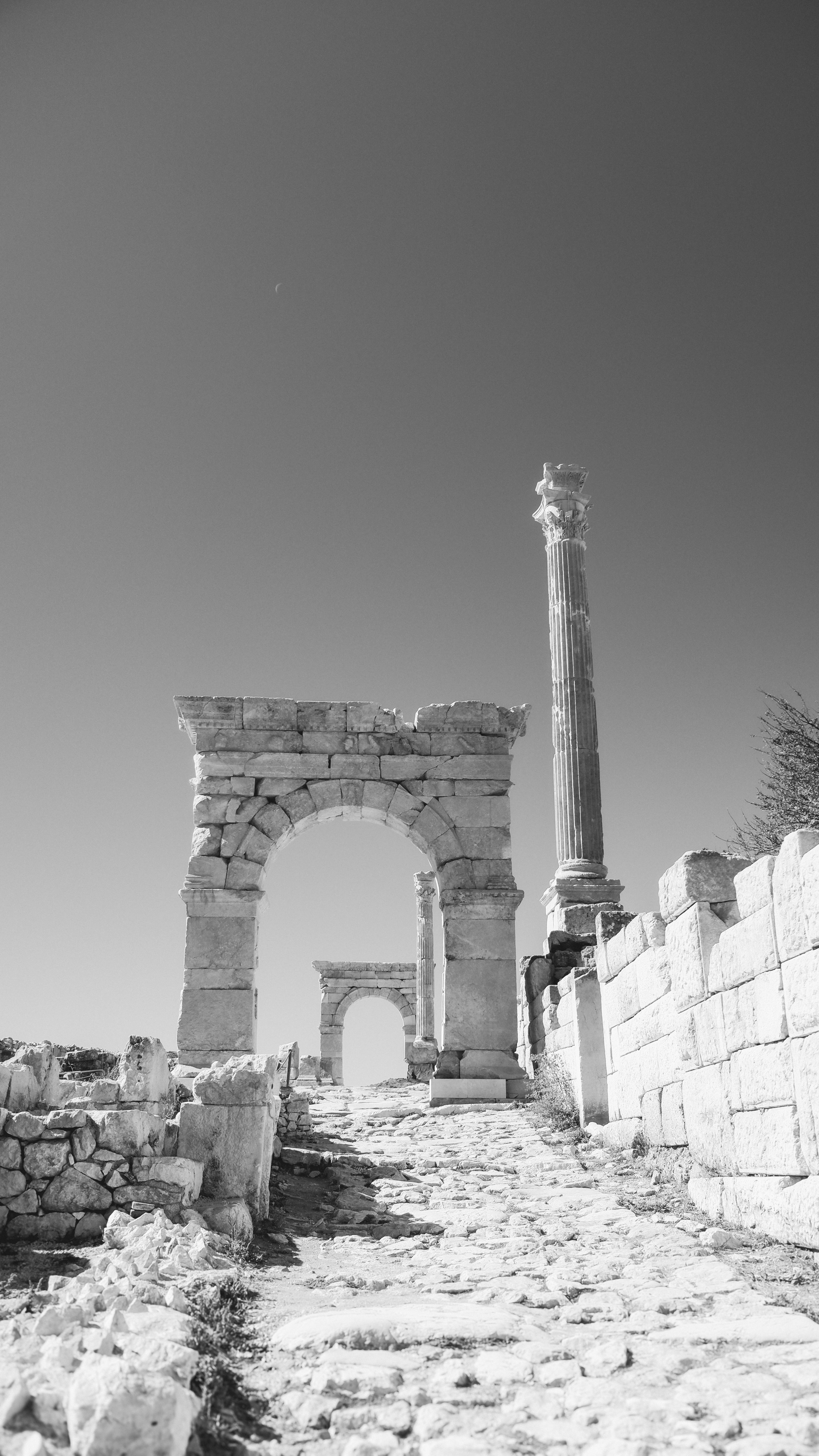 Black and white image of ancient Roman ruins with arches and a column, highlighting historical architecture.