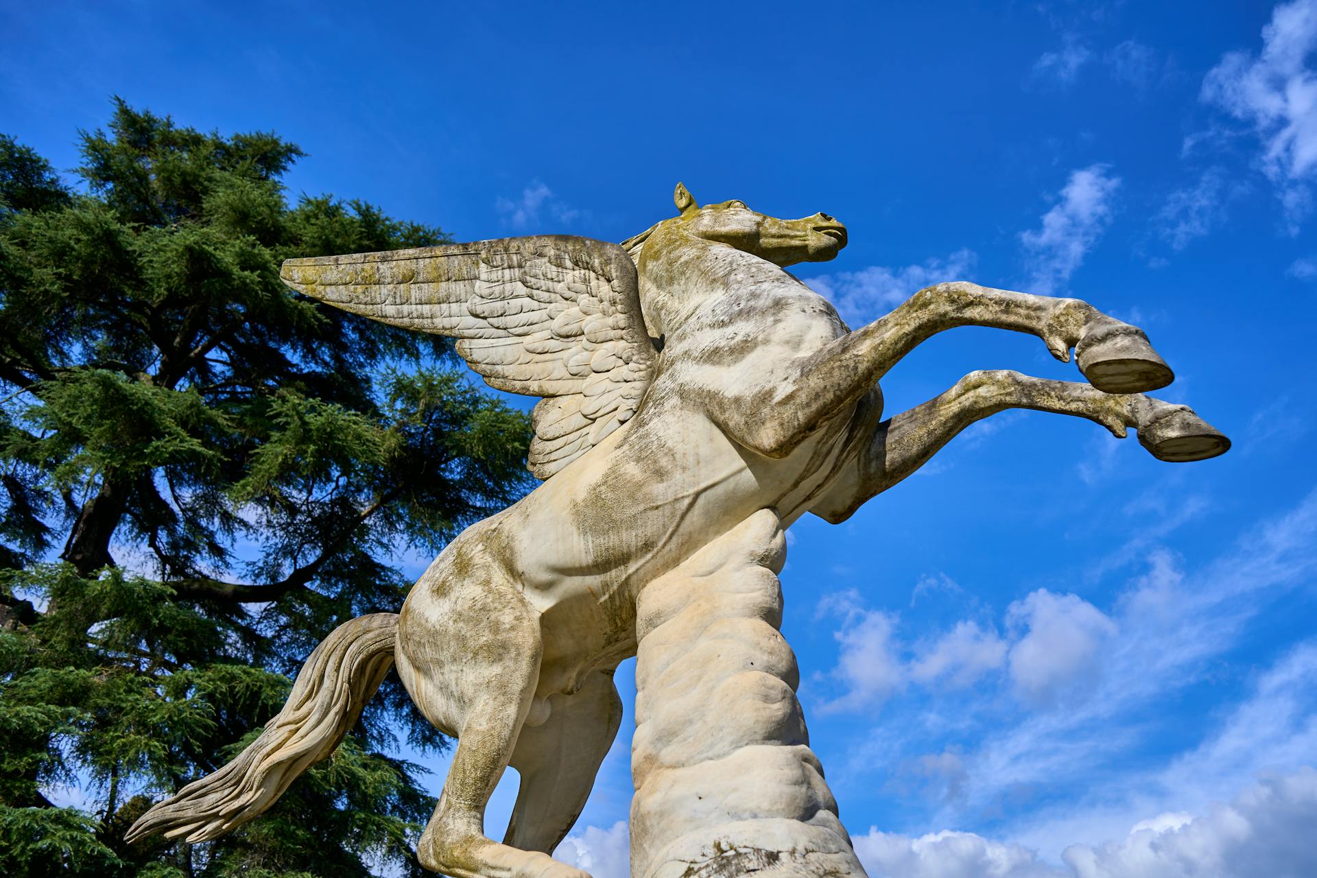 Close-up of a Pegasus statue with wings extended, set against a vibrant blue sky.