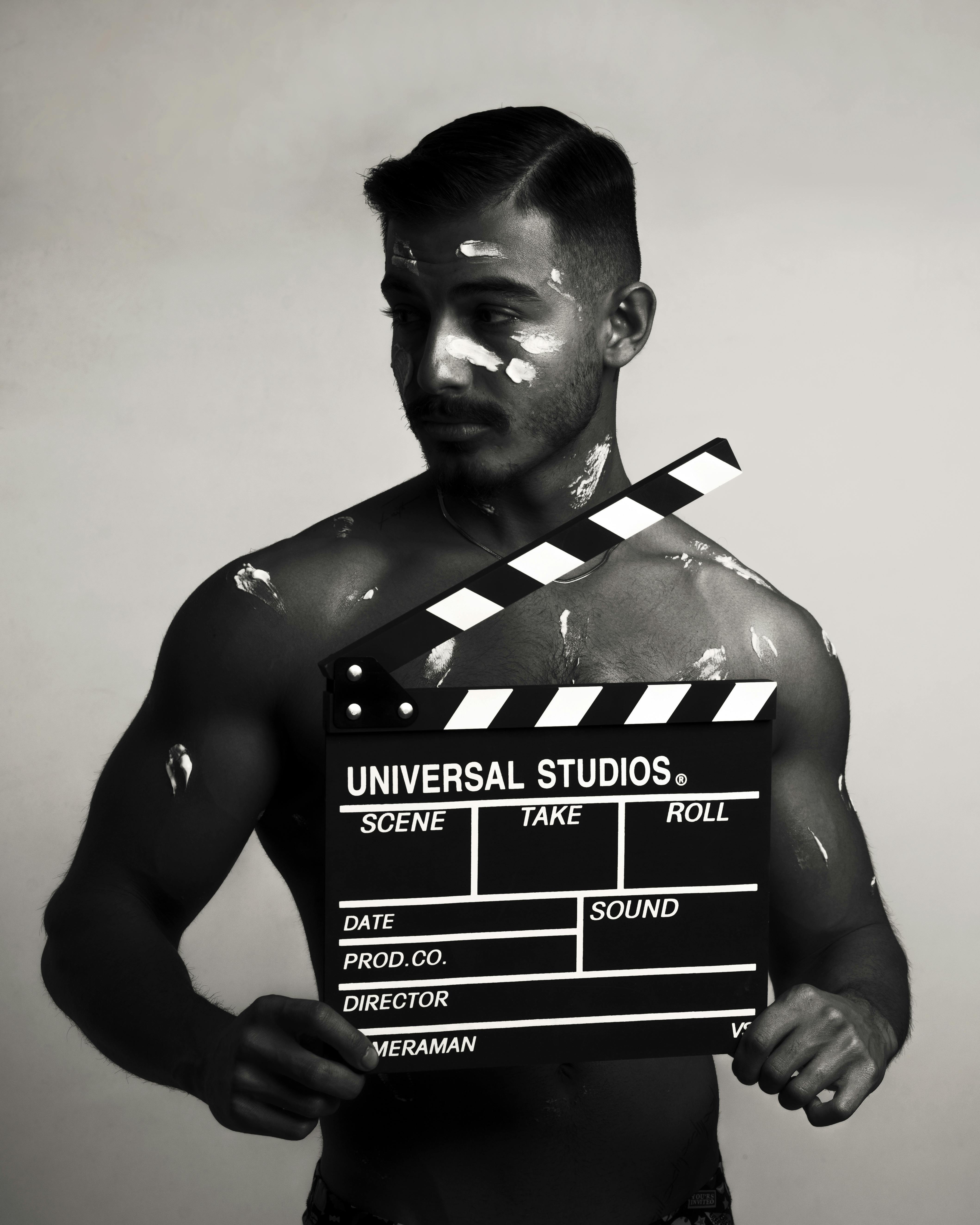 Artistic black and white photo of a muscular adult holding a movie clapperboard.