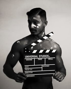 Artistic black and white photo of a muscular adult holding a movie clapperboard.