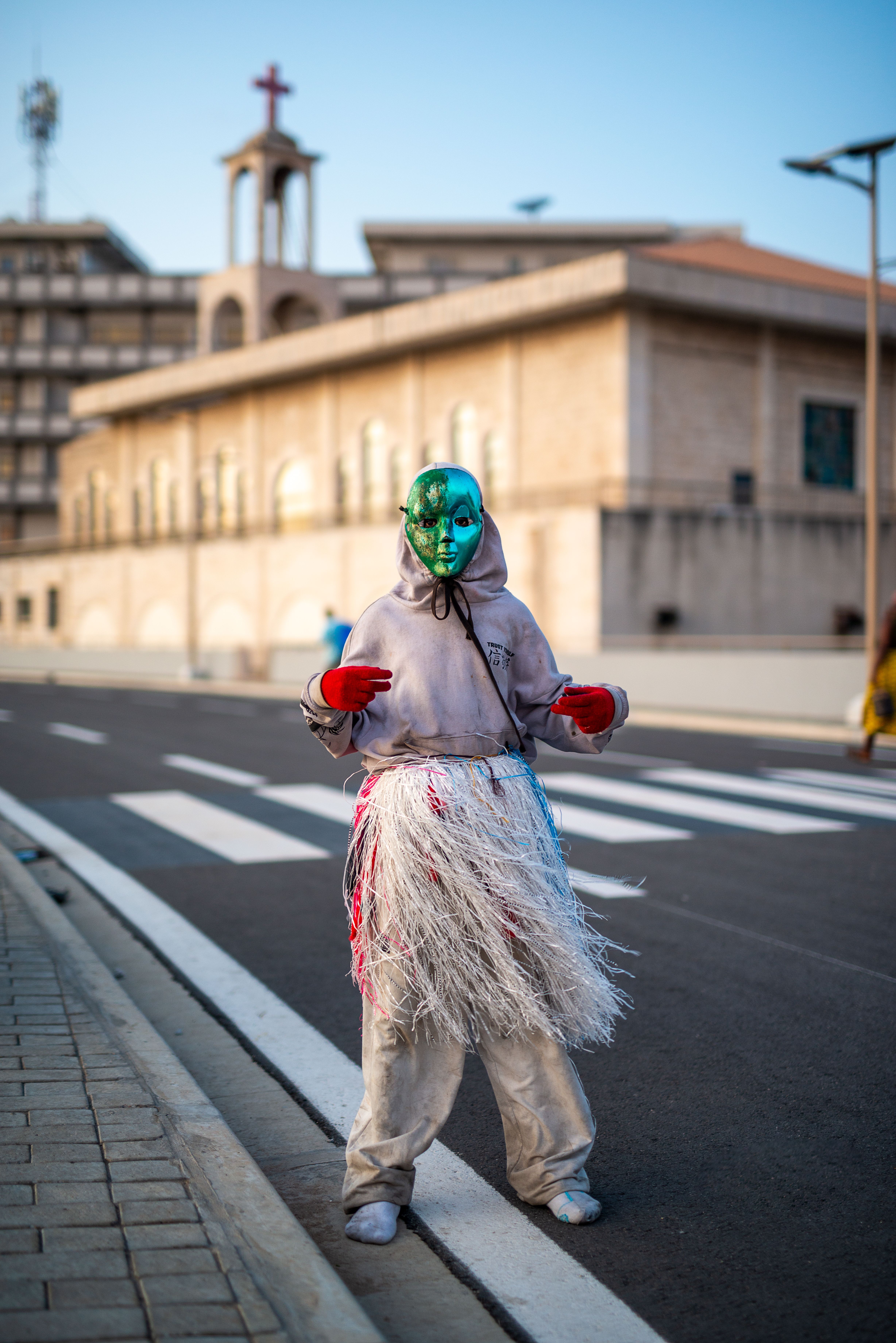 A colorful masked performer dances on an empty street in Bénin, showcasing vibrant cultural attire.