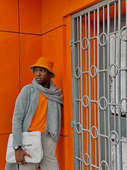 Fashionable person in orange attire poses by a colorful wall, showcasing modern street style.