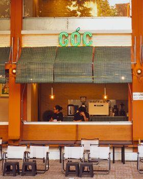 A vibrant cafe with neon signage, outdoor seating, and people enjoying coffee in Ho Chi Minh City, Vietnam.