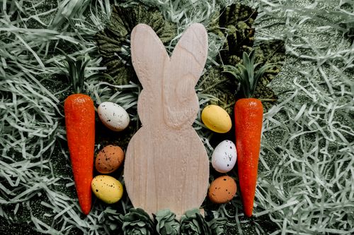 Free Decorative wooden bunny with Easter eggs and carrots on green grass. Stock Photo