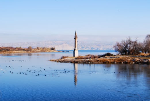 Serene waterscape in Türkiye featuring a solitary minaret reflection with a clear blue sky backdrop.