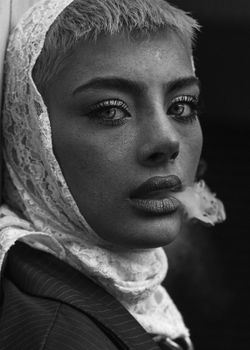 Dramatic black and white portrait of a person exhaling smoke, wearing a lace scarf.