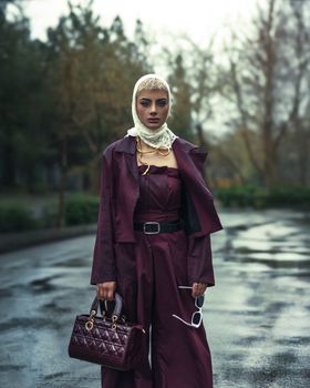 Stylish woman in burgundy outfit stands confidently on a wet street after rain, exuding elegance.