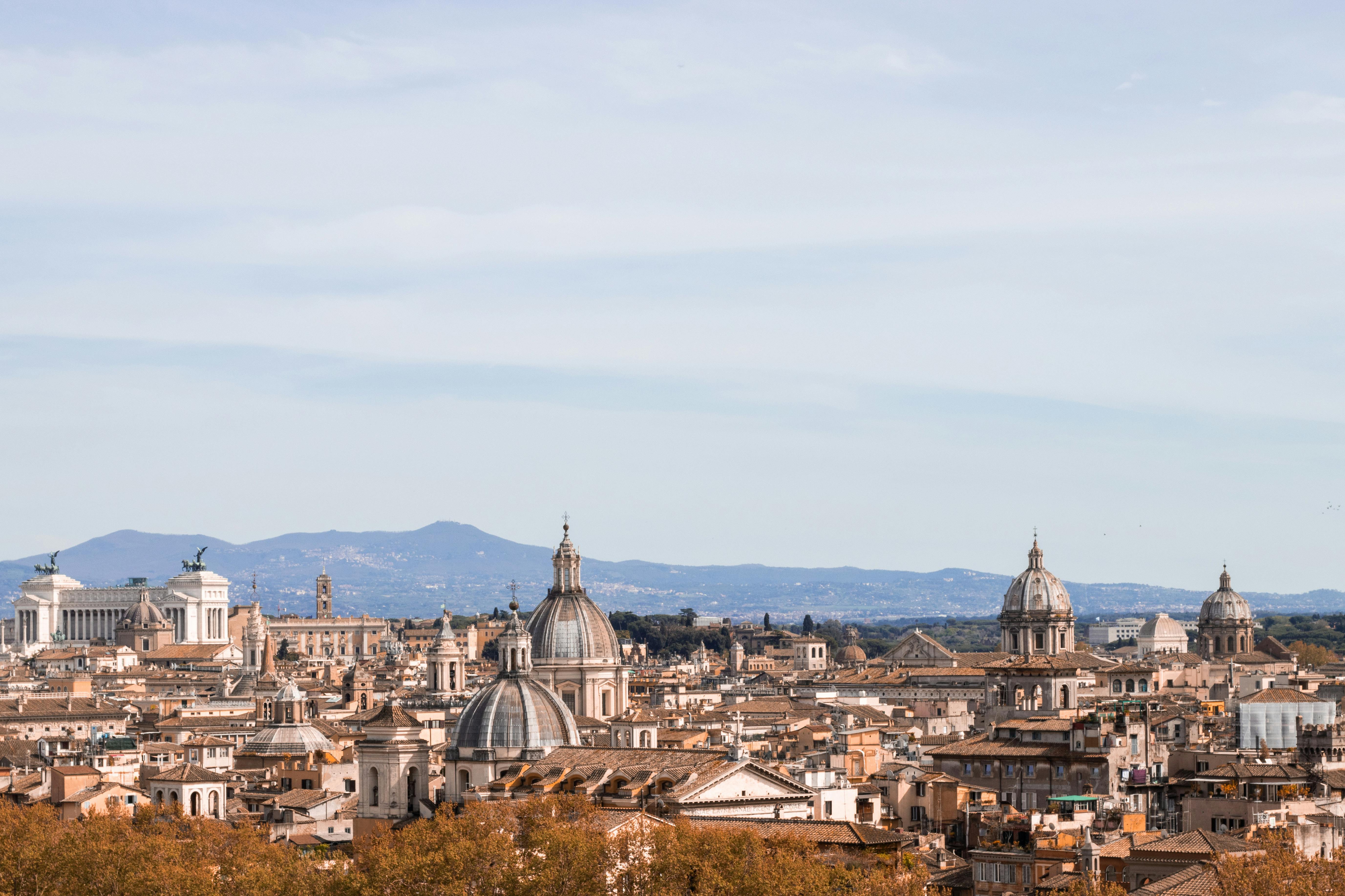 Panoramic view of Rome from Janiculum Hill showing the city's iconic skyline with Renaissance domes, terracotta rooftops, and historic monuments stretching to the horizon under a golden sky