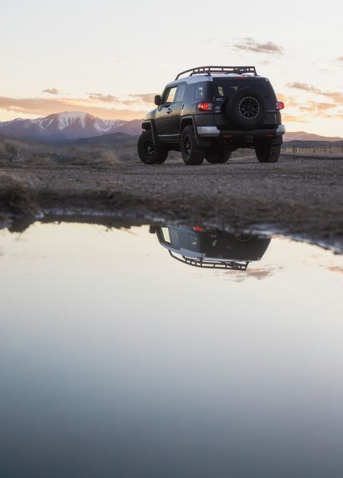 Free Off-road SUV by a mountain reflecting in a calm water pool during sunset. Stock Photo