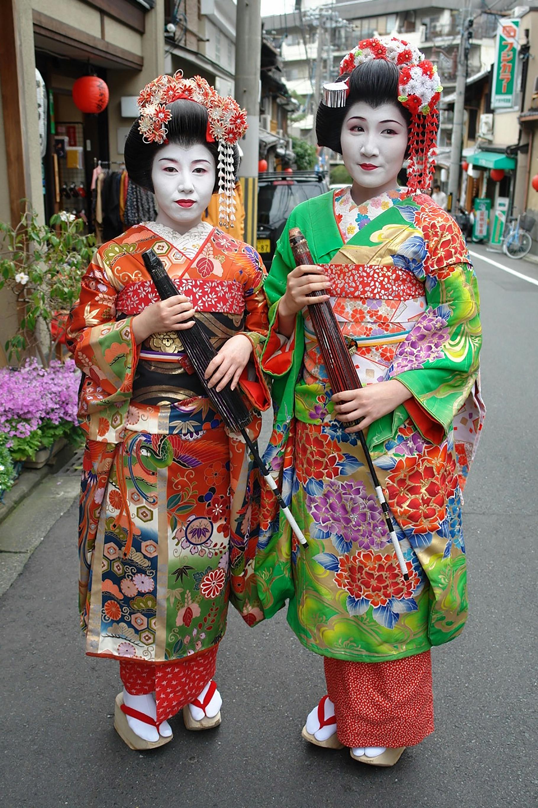 Two geisha in vibrant kimonos, posing on a street in Kyoto, Japan, showcasing cultural beauty.
