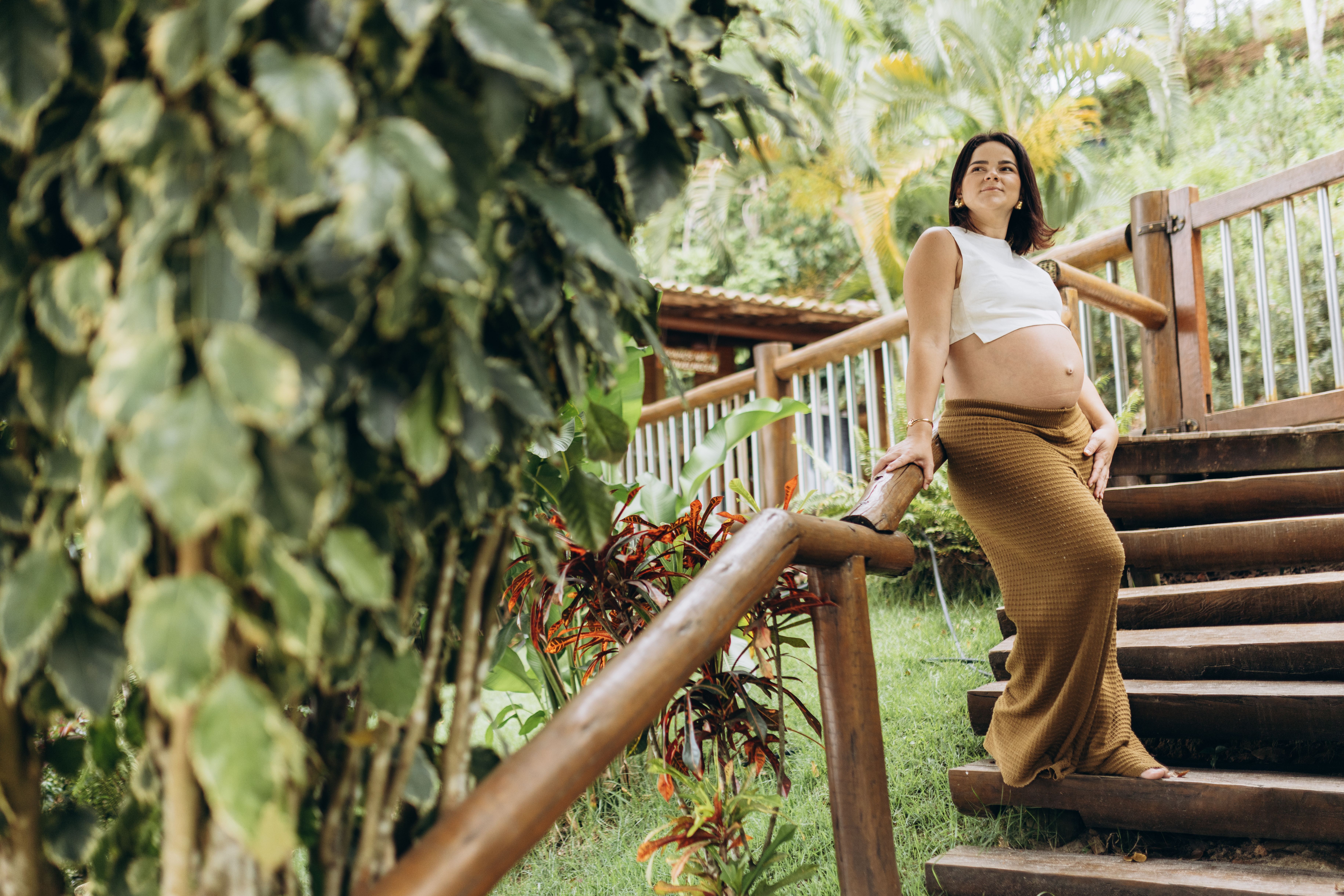 Pregnant woman enjoying a serene moment on wooden stairs surrounded by lush plants.