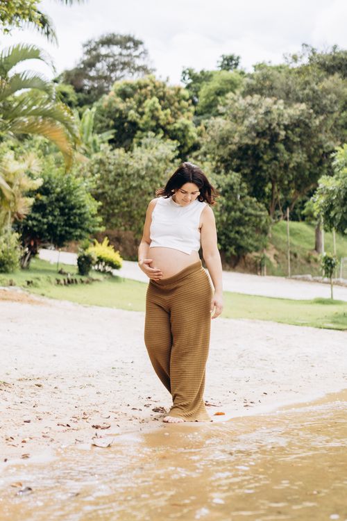 Free A pregnant woman in casual attire strolling by the water on a peaceful beach. Stock Photo