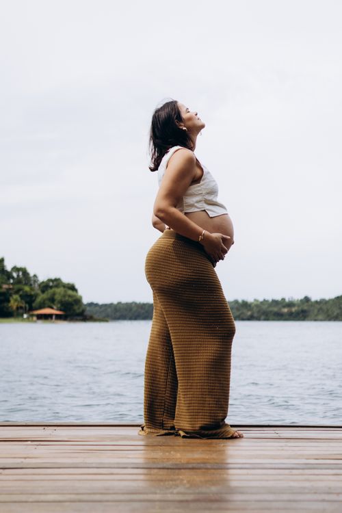 Free A pregnant woman stands by a tranquil lake, embracing nature and serenity. Stock Photo