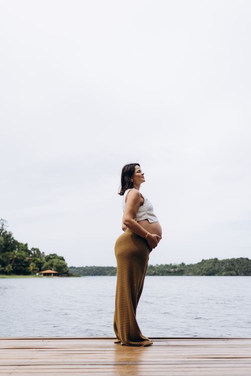 Free Profile view of a pregnant woman by a serene lake, embracing nature. Stock Photo