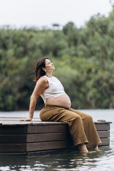 A serene moment of a pregnant woman enjoying nature by a lake.