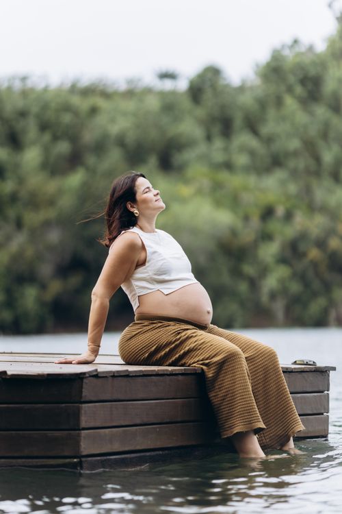 Free A serene moment of a pregnant woman enjoying nature by a lake. Stock Photo