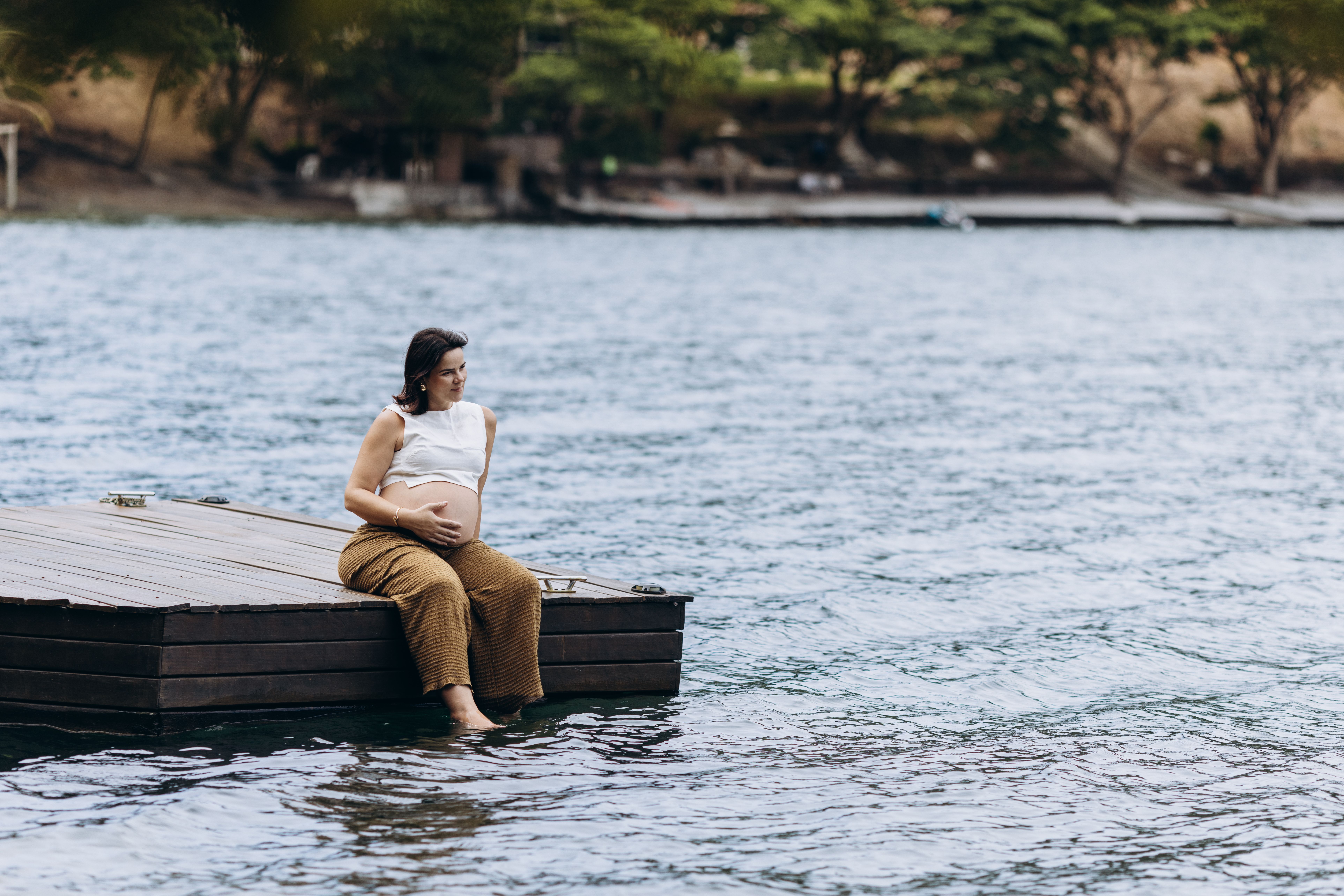 Expectant mother enjoying serene lake view while sitting on a dock.