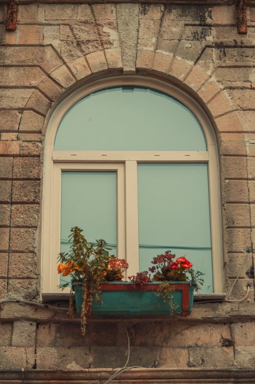 Free Vintage arched window with a vibrant flower planter, adding charm to the textured stone facade. Stock Photo