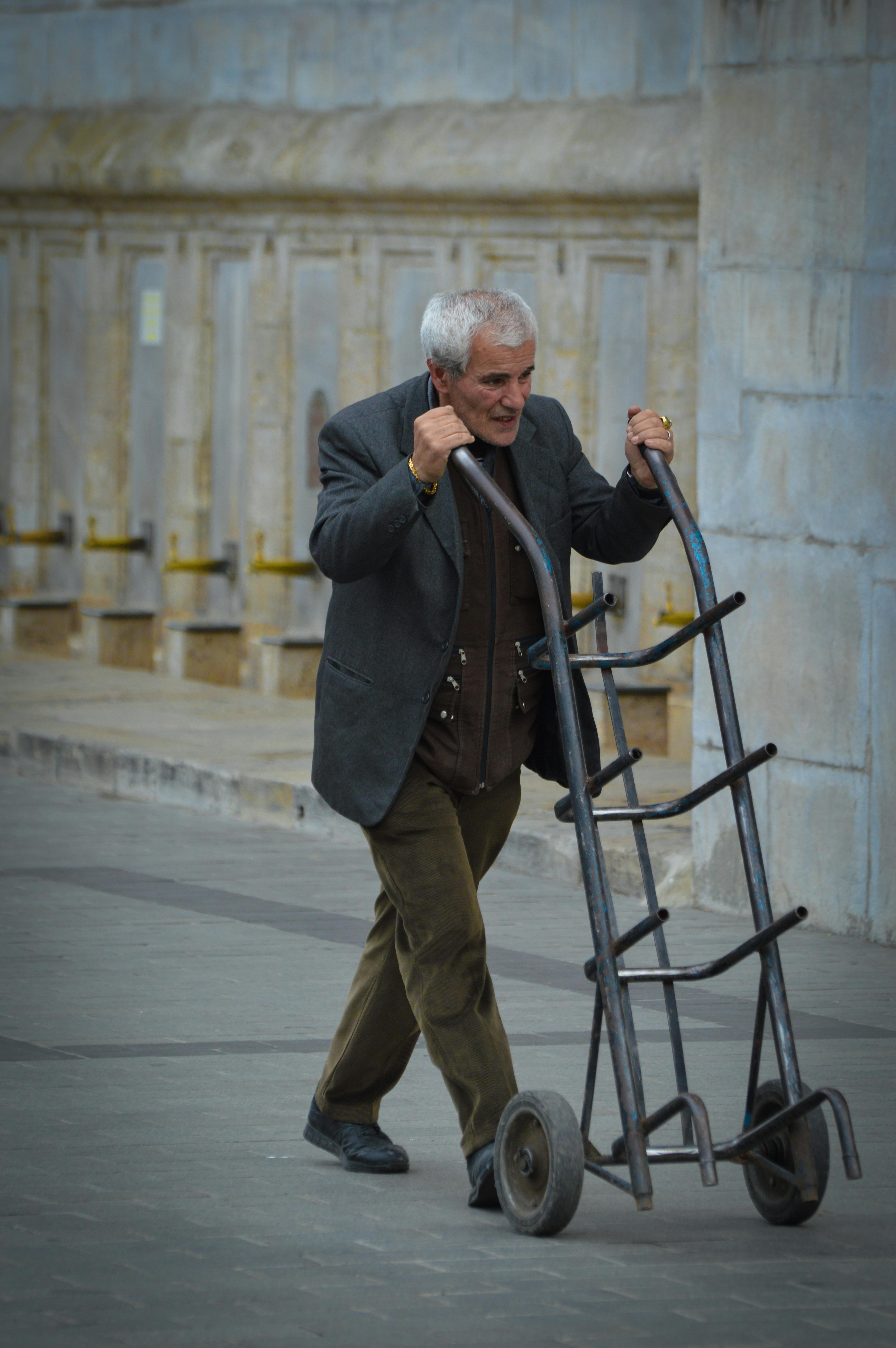 Senior man pushing an empty hand truck outdoors in an urban setting.