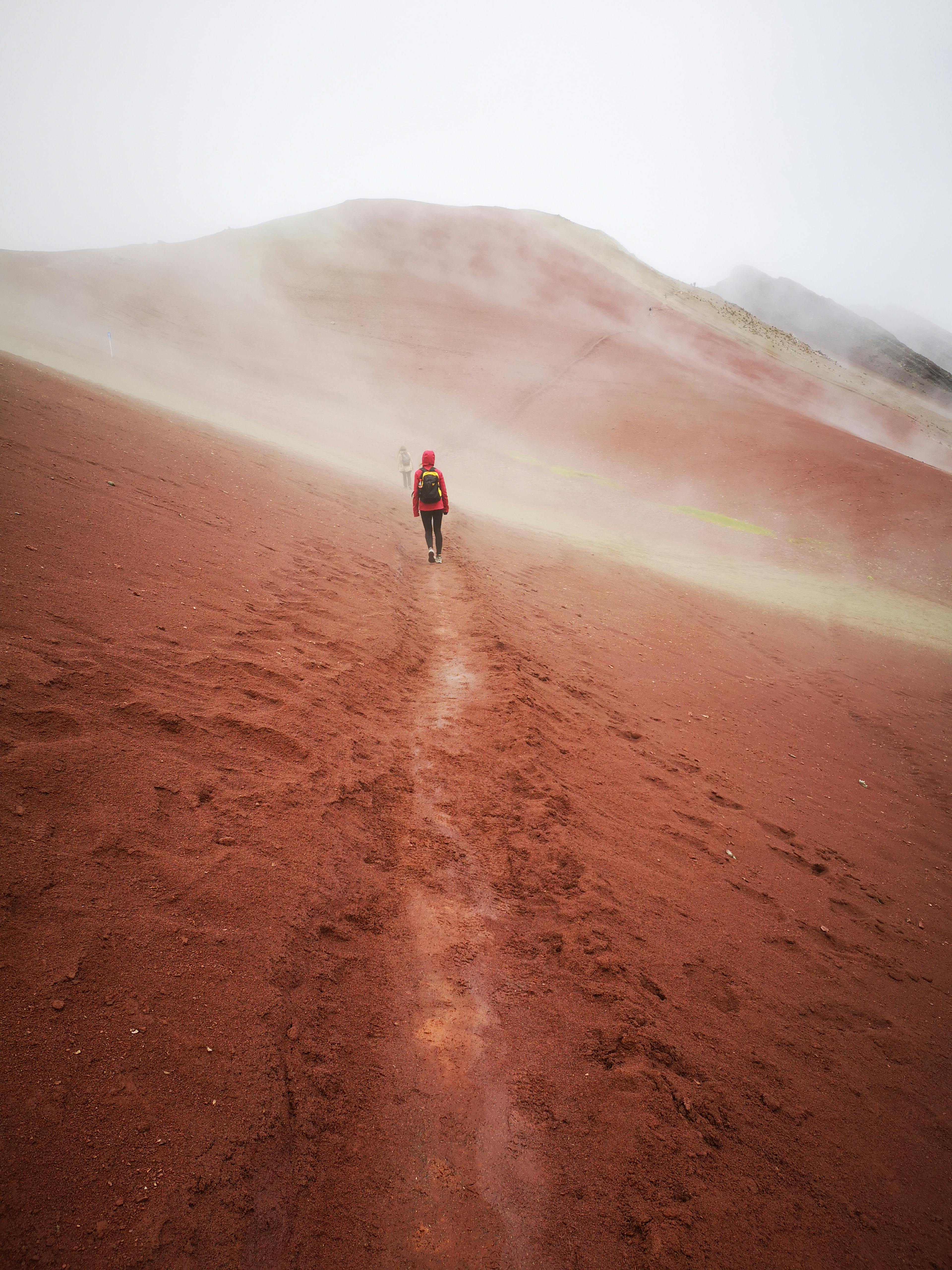 A solitary traveler explores a misty, red sand trail in the unique landscapes of Peru's scenic countryside.