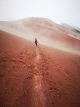 A solitary traveler explores a misty, red sand trail in the unique landscapes of Peru's scenic countryside.