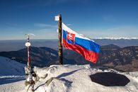 Slovak flag atop a snowy mountain with a panoramic view of distant ranges.