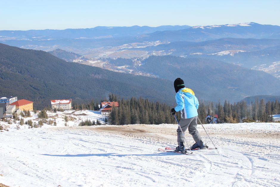 A lone skier glides down a picturesque snowy slope with mountain views and clear blue skies, capturing the essence of winter adventure.