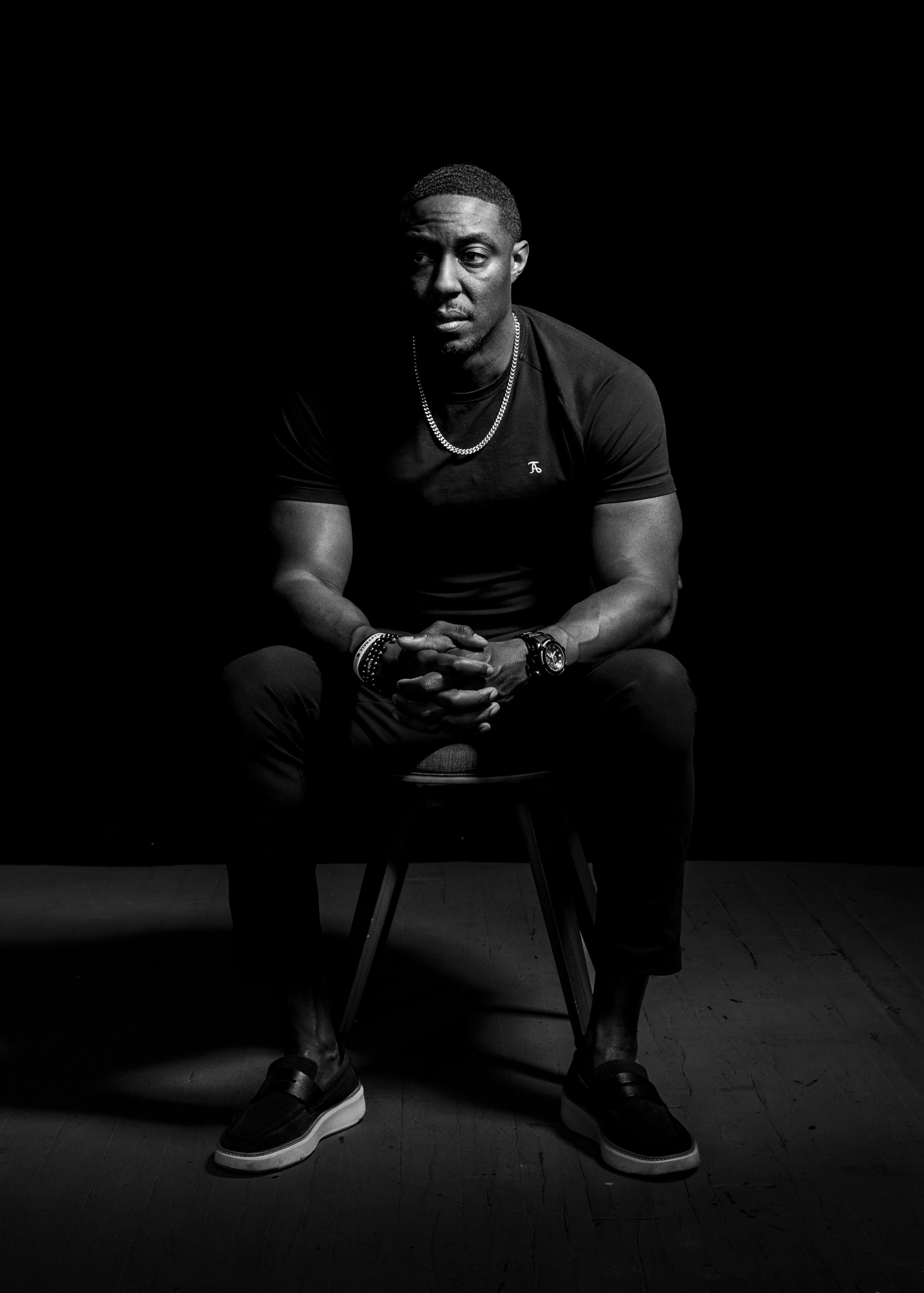 Striking black and white portrait of a man seated in a contemplative pose, with dramatic lighting and shadows.