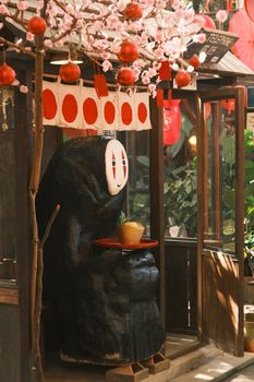 Statue under cherry blossoms in Japanese decor with red lanterns.