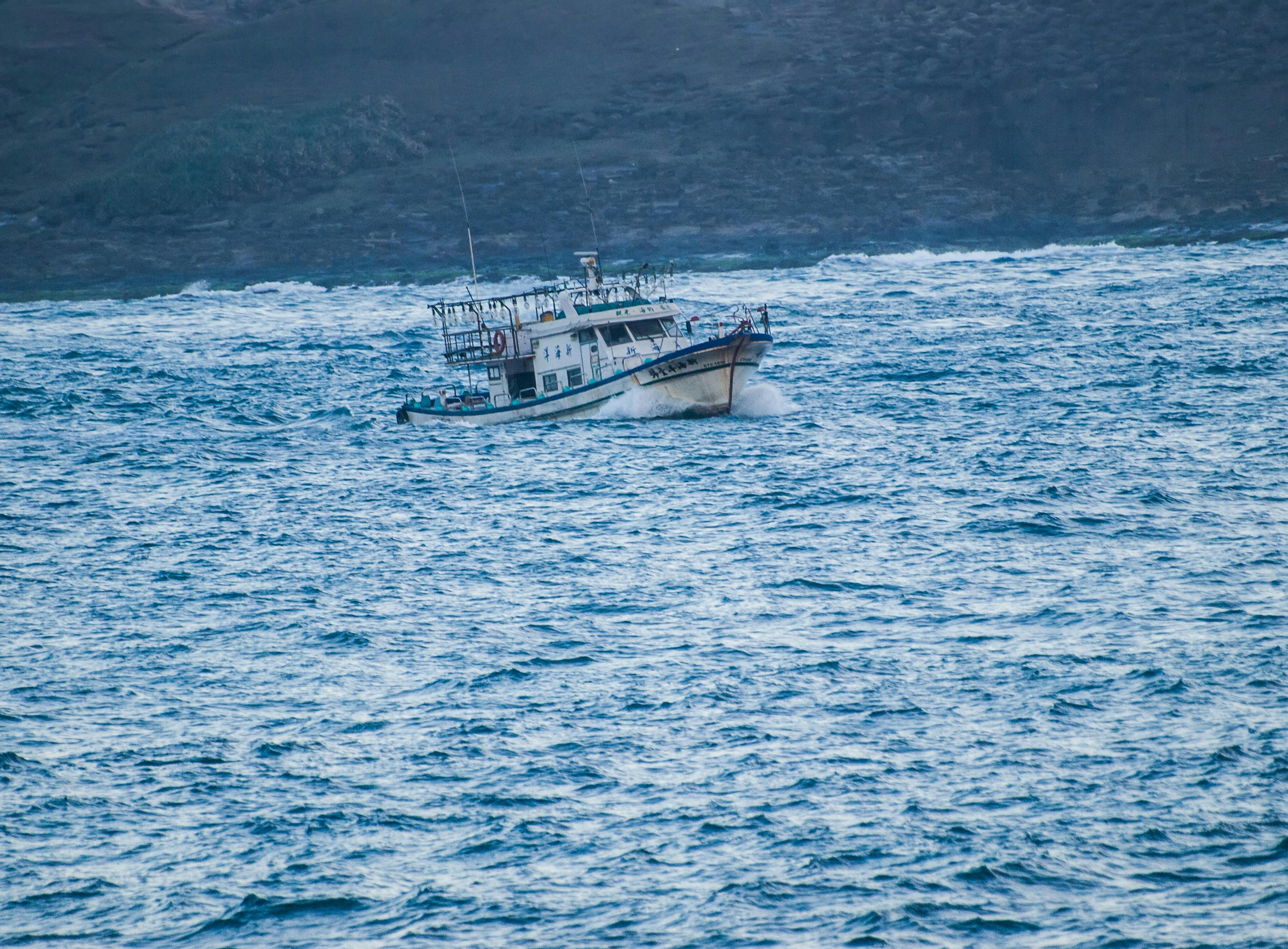 A fishing boat sails through choppy ocean waves near a rocky coastline, capturing maritime adventure.