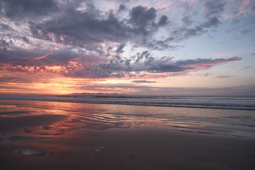 Free Peaceful beach at sunrise with vibrant clouds and calm waves. Stock Photo
