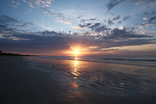 Peaceful sunset view over a calm beach with reflections and gentle waves.