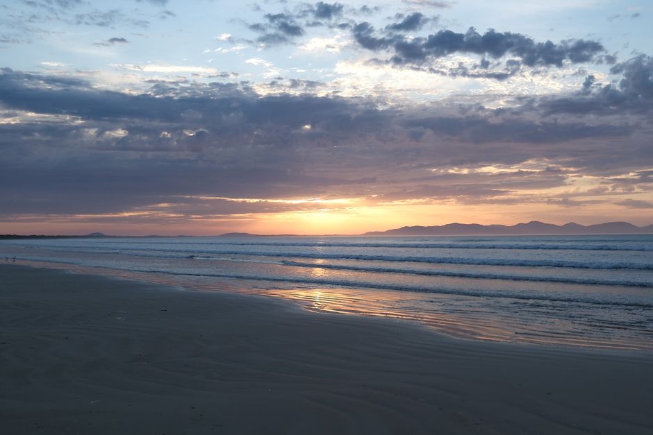 Serene ocean sunrise with colorful sky over a tranquil beach, perfect for relaxation themes.