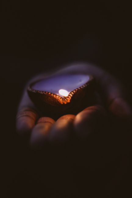 A diya lamp glows warmly in a human hand, symbolizing light and tradition.